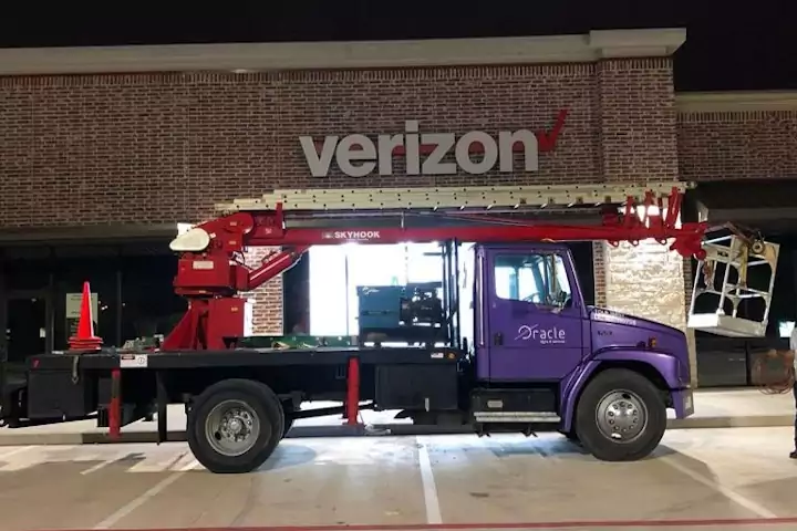 Oracle Signs Texas - Exterior wall sign installation of a verizon store. Picture shows a purple truck with a crane on the bed. The verizon sign is visible in the background