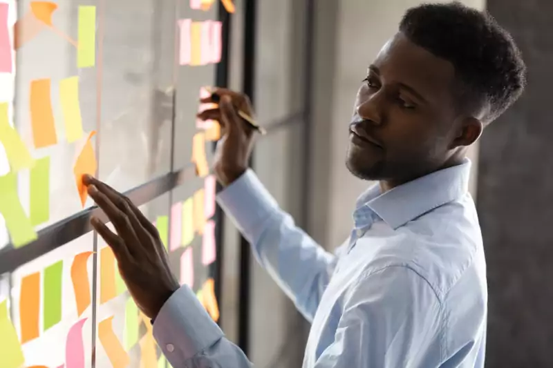 Oracle Signs Texas - Image of a black man standing in front of a pane of glass managing several sticky notes. Working on project management